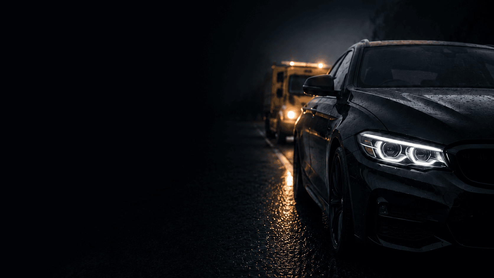 A dark luxury saloon on a wet road at night, with a yellow recovery vehicle's lights behind it
